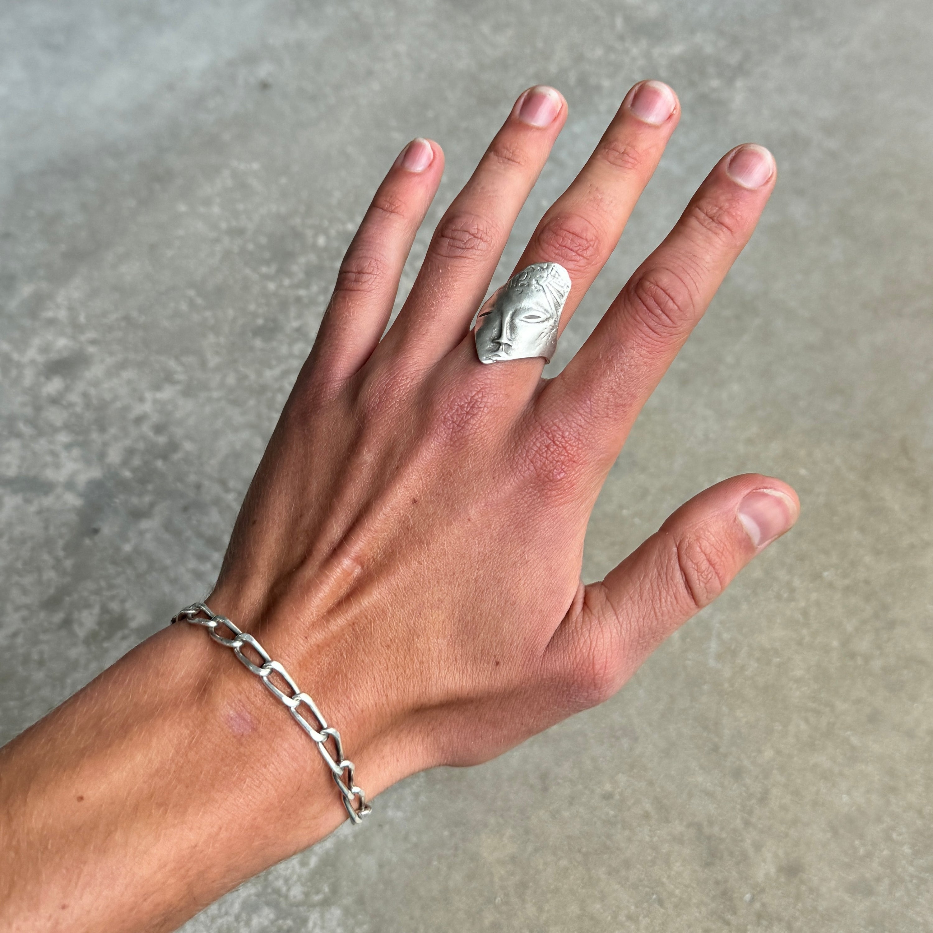 a photo of a hand with an abstract face silver ring on it