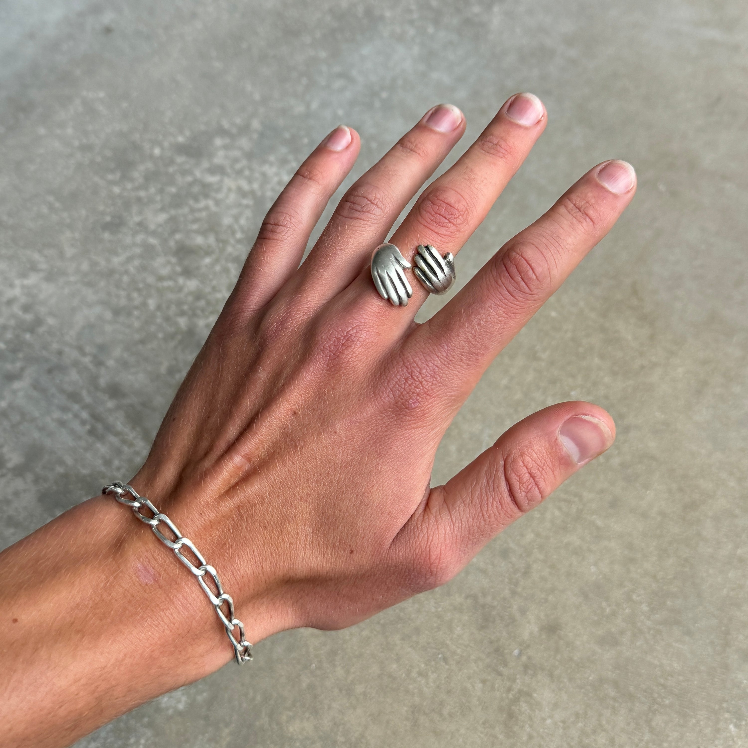 a photo of a silver ring with a double hugged hands design on a hand