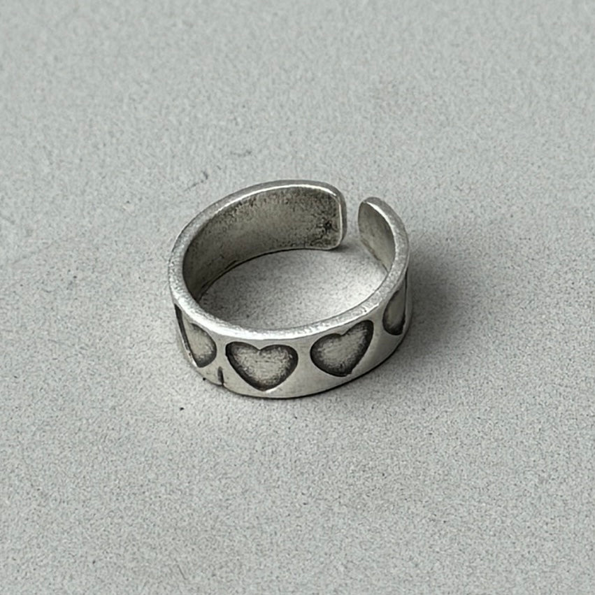 a photo of the back of a silver ring with a stamped hearts design and vintage silver finish