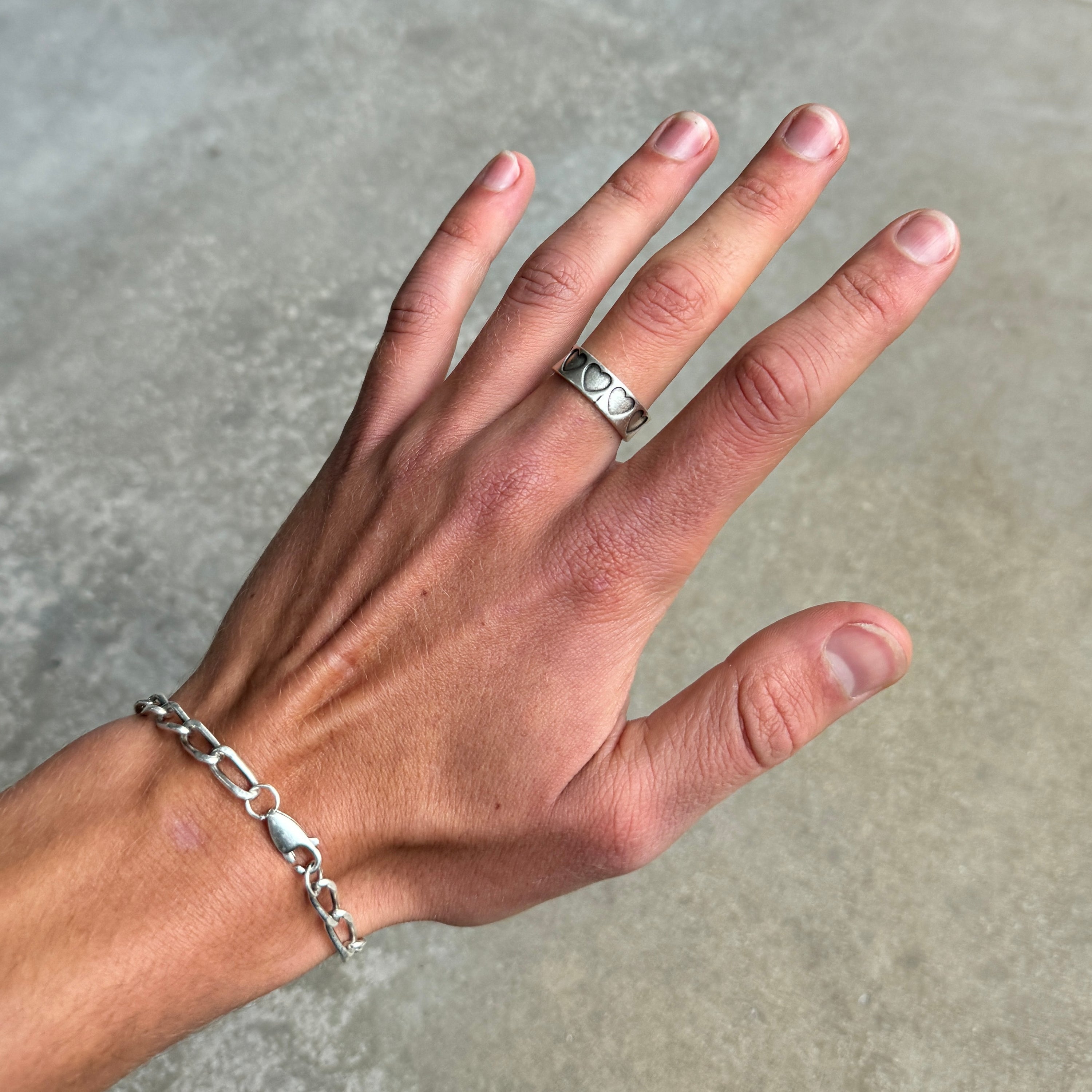 a photo of a hand wearing a silver ring with a stamped hearts design and vintage silver finish