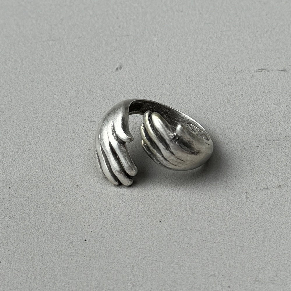 a photo of a silver ring with a double hugged hands design