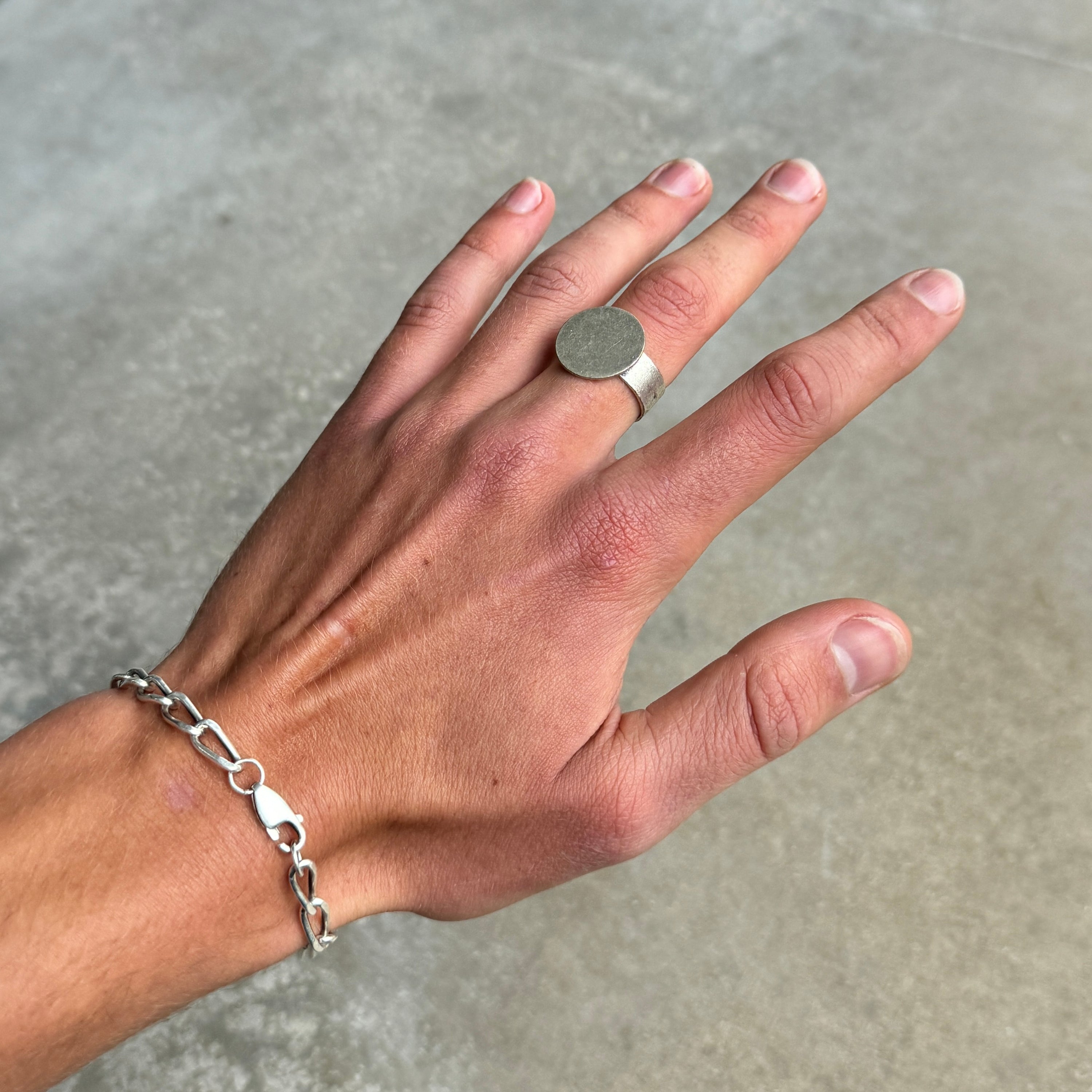 photo of a hand wearing a silver ring with an oversized circle design and antique style finish to the silver