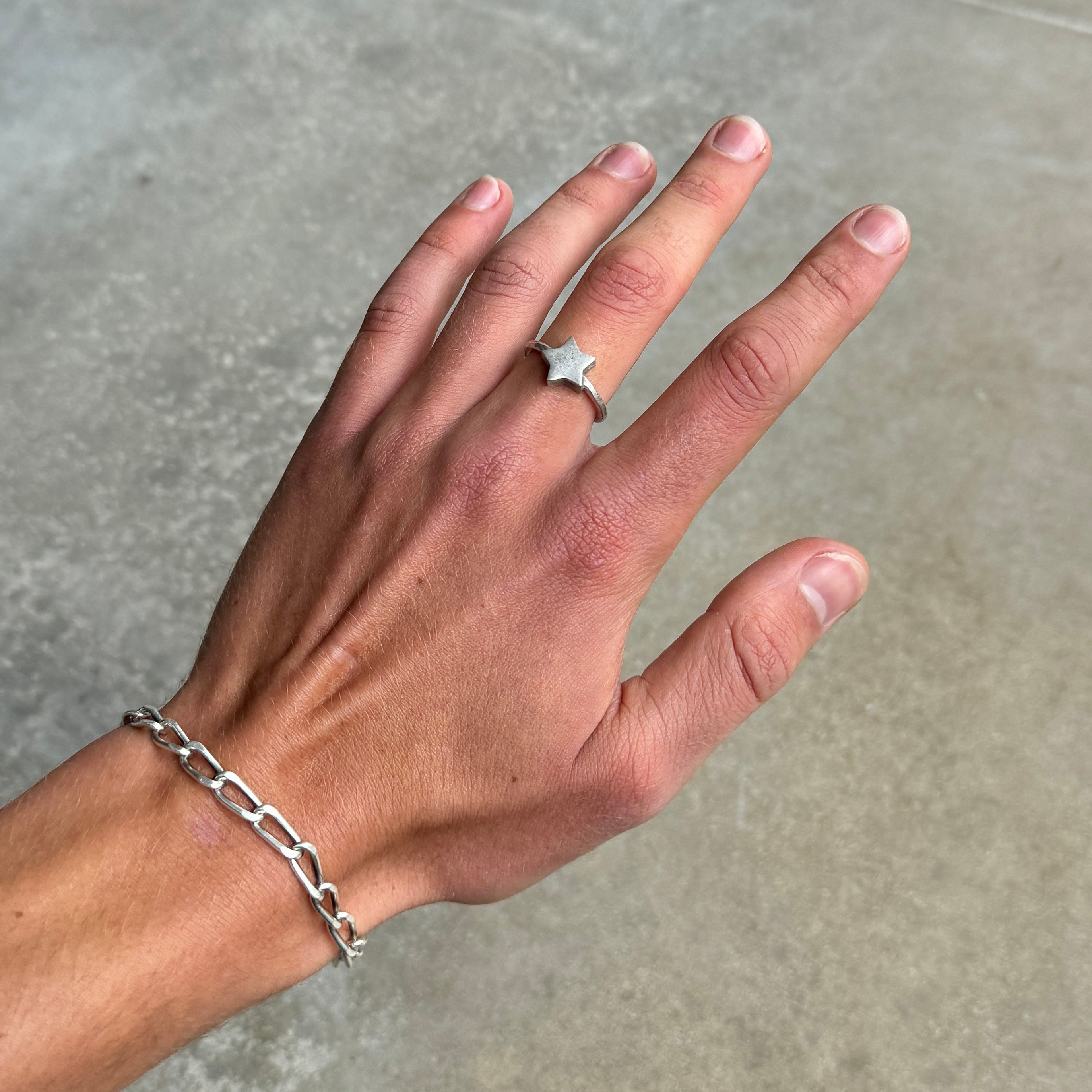 a photo of a hand wearing a silver ring with a simple star design and vintage style finish to the silver